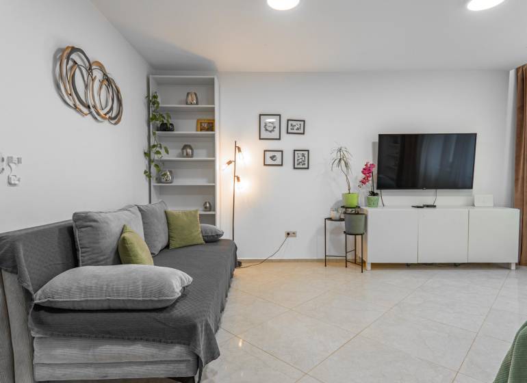 I Luxusný byt v historickom centre Bratislavy - Obývačka v 2-izbovom byte s TV, pohovkou a minimalistickou dekoráciou na bielej stene.