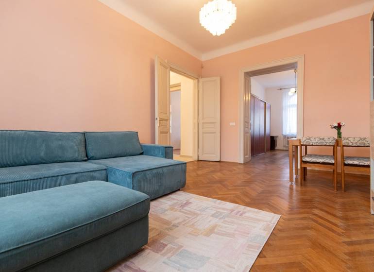 3-izbový byt s vysokými stropmi, Staré Mesto - Izba v 3-izbovom byte s modrou sedačkou, dreveným dekorom podlahy a jedálenským kútom.