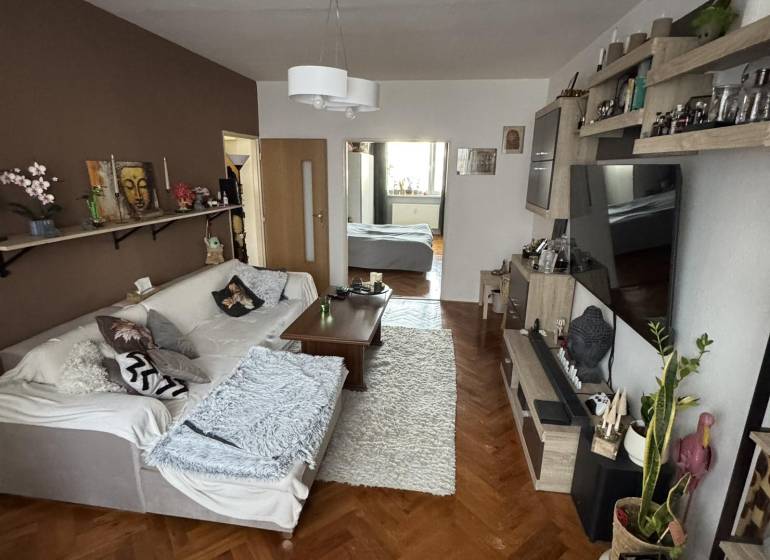 PREDAJ: 3-izbový byt 77 m², Šahy – Výborná investícia aj bývanie  - Obývačka so sedačkou, stolom a podlahou s dreveným dekorom v 3-izbovom byte.