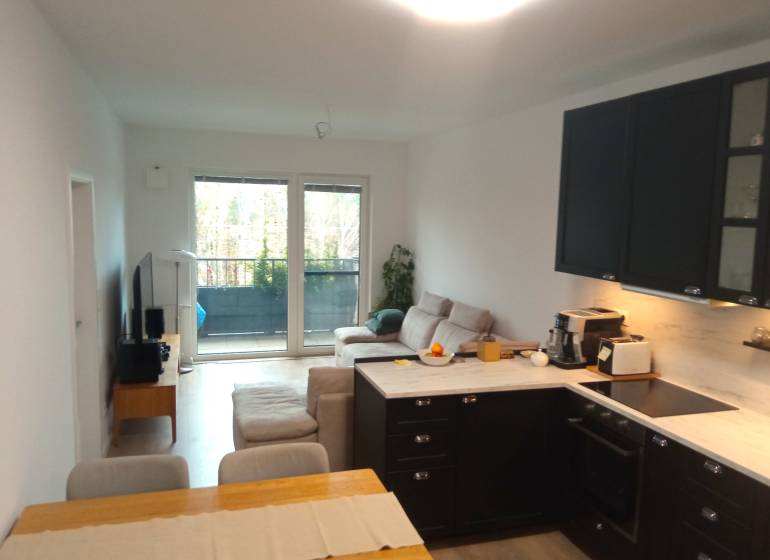 VÝMENA! Nový 2+kk s park. miestom a lodžiou za 3+1, Rača, Bratislava - Interiér 2-izbového bytu s kuchyňou, pohovkou a balkónom, podlaha s dreveným dekorom.