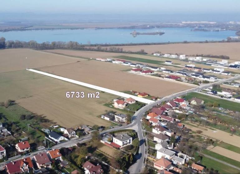INVESTIČNÝ POZEMOK 6733 m² NA RD – SOKOLOVCE (okres Piešťany) - Pozemky na bývanie v Sokolovciach, okolitá krajina s vodnou plochou v pozadí.