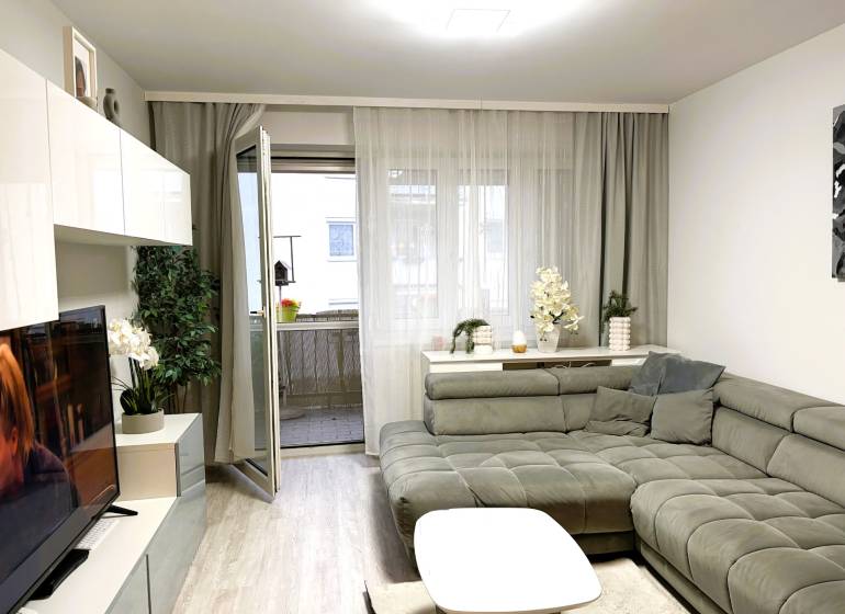 3 izbový byt s balkónom v obľúbenej lokalite Neusiedl am See - Obývačka v 3-izbovom byte s pohodlným sedačkovým kútom a podlahou s dreveným dekorom.