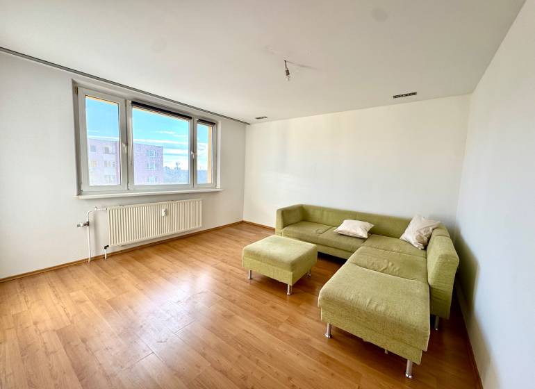 Zrekonštruovaný 3i byt na začiatku Petržalky, električka, les, výhľady - Obývacia izba v 3-izbovom byte s podlahou s dreveným dekorom a zelenou sedačkou.