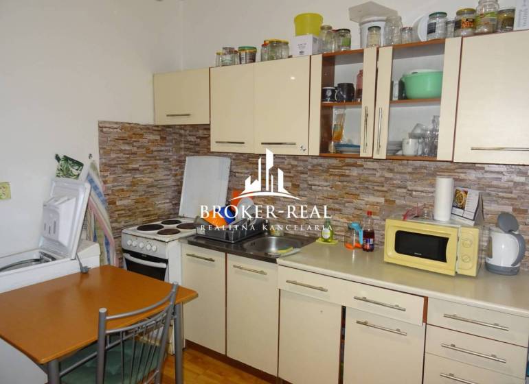 1 - izbový byt Košice, Popradská - Kuchyňa v 1-izbovom byte s kuchynskou linkou, spotrebičmi a dreveným dekorom podlahy.