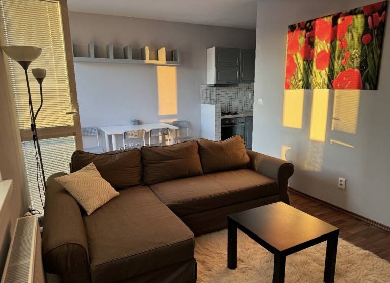 Prenájom 2-izb byt v uzavretom areáli Bratislava II - Obývacia izba s hnedou sedačkou, stolíkom a podlahou s dreveným dekorom v 2-izbovom byte.