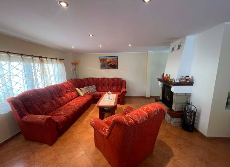 PREDAJ - Zrekonštruovaná rekreačná chata - Chľaba - Obývacia izba s krbom, červeným gaučom a podlahou s dreveným dekorom v chate.