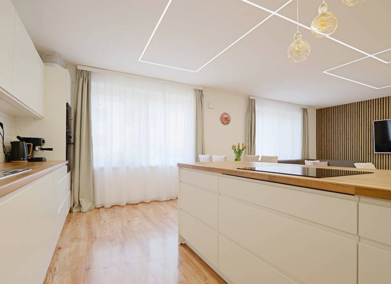 TOP - Rodinný dom s veľkým pozemkom - Dolný Hričov - Kuchyňa v Rodinnom dome s podlahou s dreveným dekorom, svetlým nábytkom a veľkým oknom.