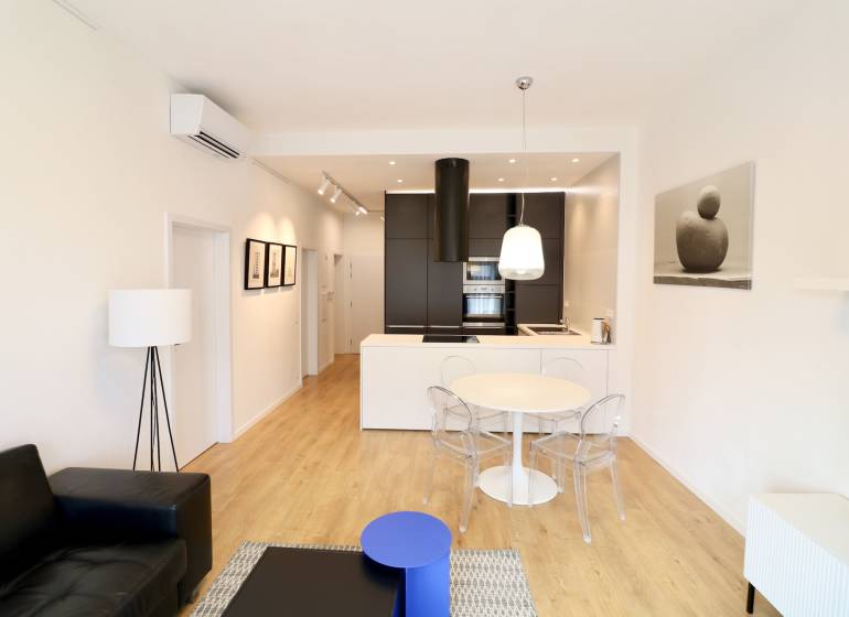 Komfortne vybavený 2-izbový byt v projekte 2 Sýpky - Obývacia izba s podlahou s dreveným dekorom, kuchynskou linkou a jedálenským stolom v 2-izbovom byte.