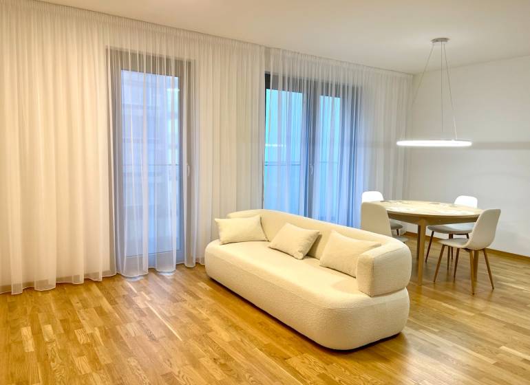 I 3 i byt s parkovaním v rezidenčnom komplexe METROPOLIS - Obývacia izba s béžovou pohovkou, okrúhlym stolom a podlahou s dreveným dekorom.