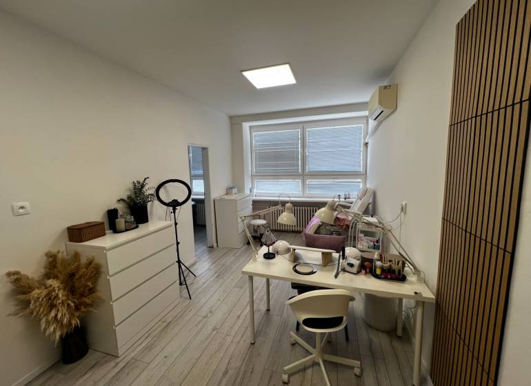 Prenájom ordinácie v zdravotnom stredisku Saratovská 24, Bratislava. - Biela miestnosť s pracovným stolom, lampami a dekoráciou na podlahe s dreveným dekorom.