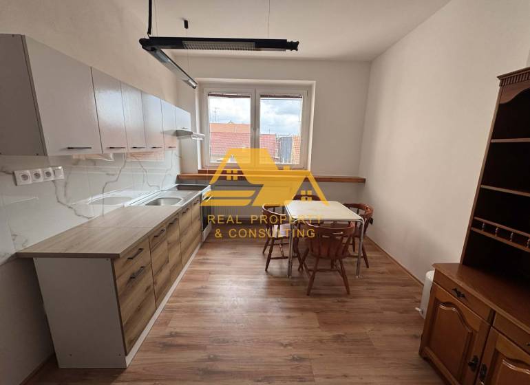 Prenajmem 1 izbový byt v Nových Zámkoch - Kuchyňa v 1-izbovom byte so stolom, stoličkami a podlahou s dreveným dekorom.