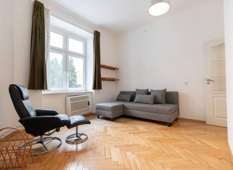 Priestranný 4-izbový byt s predzáhradkou, Staré Mesto - Svetlá obývacia izba s podlahou s dreveným dekorom v 4-izbovom byte, sivá sedačka, kreslo.