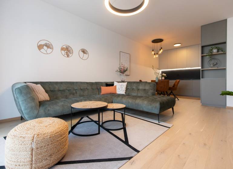2-izbový byt s lodžiou v projekte Zwirn - Obývacia izba v 2-izbovom byte s pohovkou, konferenčnými stolíkmi a podlahou s dreveným dekorom.