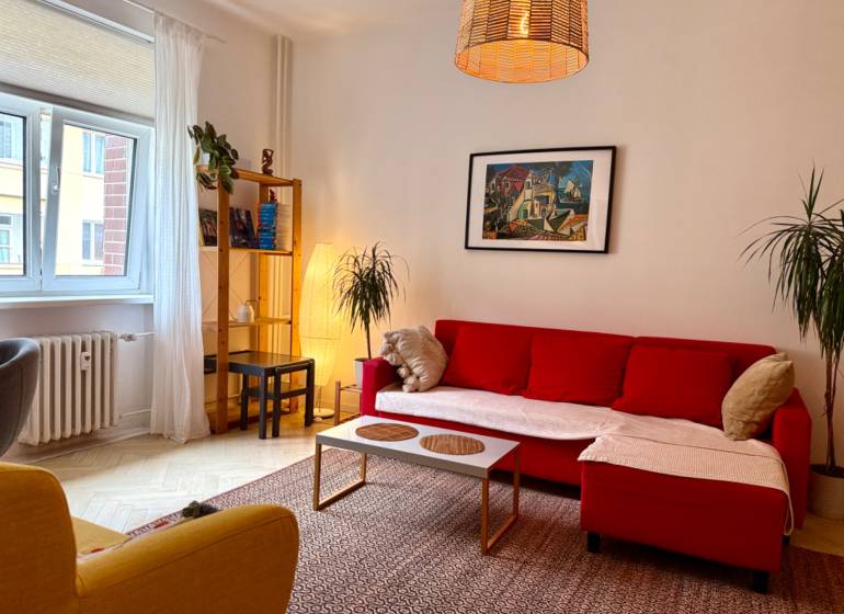 Na prenájom 2 izbový byt, Bratislava, Staré Mesto, Wilsonova ulica - Obývačka 2-izbového bytu s červenou pohovkou a podlahou s dreveným dekorom.