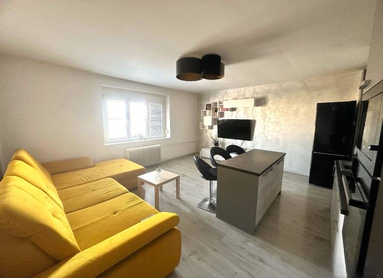Prenájom pekný 2 izbový byt Šancová ulica, Bratislava III. Nové Mesto - Obývacia izba s veľkou žltou sedačkou, kuchynským ostrovom a televíziou v 2-izbovom byte.