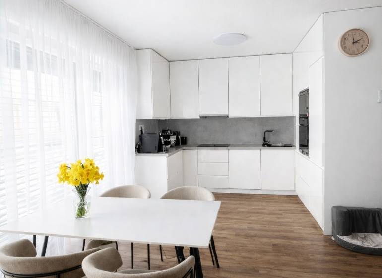 Predaj 3-izbový byt s terasou 20m2, parkovanie, Dunajská Lužná - Jedálenský stôl so stoličkami a kuchyňa v 3-izbovom byte s podlahou s dreveným dekorom.
