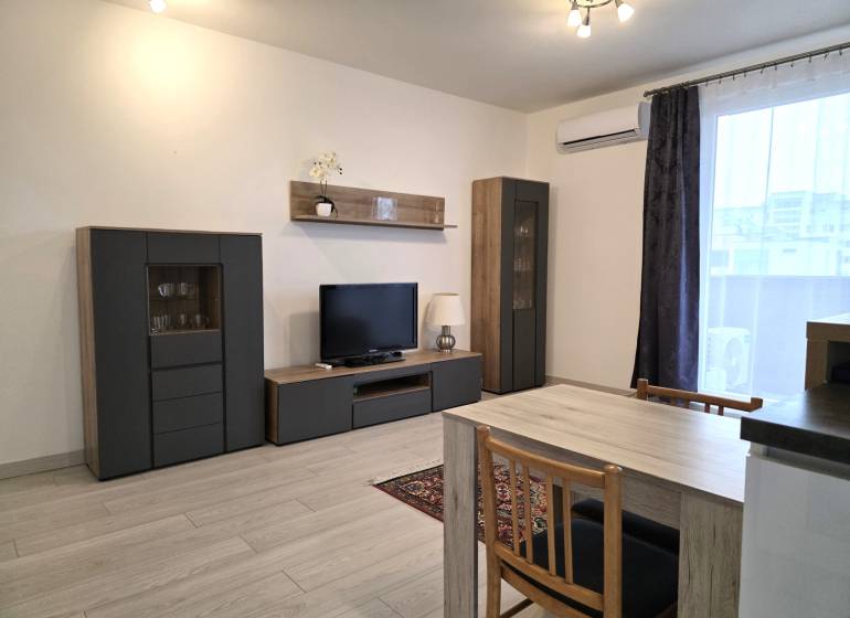 PRENÁJOM - 3 izbový byt v novostavbe - Nitra, blízko centra - Obývacia izba s TV, skrinkami, stolom a podlahou s dreveným dekorom v 3-izbovom byte.