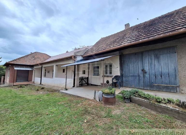 Pôvodný päťizbový rodinný dom s hospodárskymi budovami blízko centra o - Rodinný dom v Mužli s tradičnou fasádou, verandou a bujnou záhradou.