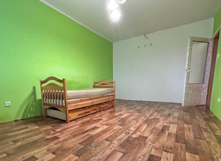 Na predaj 2i byt Levice - Izba s posteľou v 2-izbovom byte, podlaha s dreveným dekorom, zelené steny.