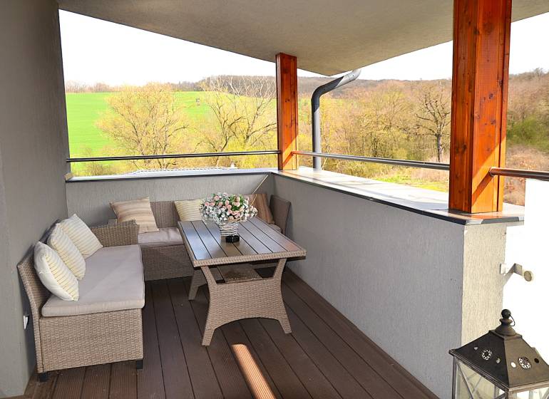 Na predaj apartmán s veľkou terasou Podhájská. - Priestranný balkón s ratanovým nábytkom a podlahou s dreveným dekorom v garsónke.