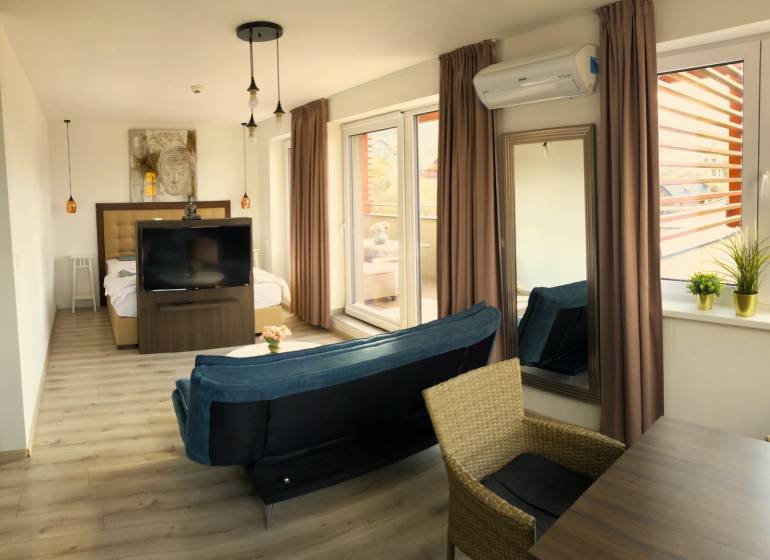 Na predaj veľký 49m2 apartmán Podhájská.  - Svetlý 2-izbový byt s podlahou s dreveným dekorom, pohovkou a veľkými oknami.