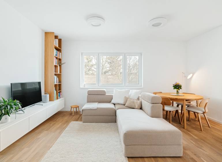 NUERA | PREDAJ 4i byt s predzáhradkou pri lese + 2x parking , BAIV - Obývacia izba so sedačkou, TV, knihovňou a jedálenským stolom, podlaha s dreveným dekorom.