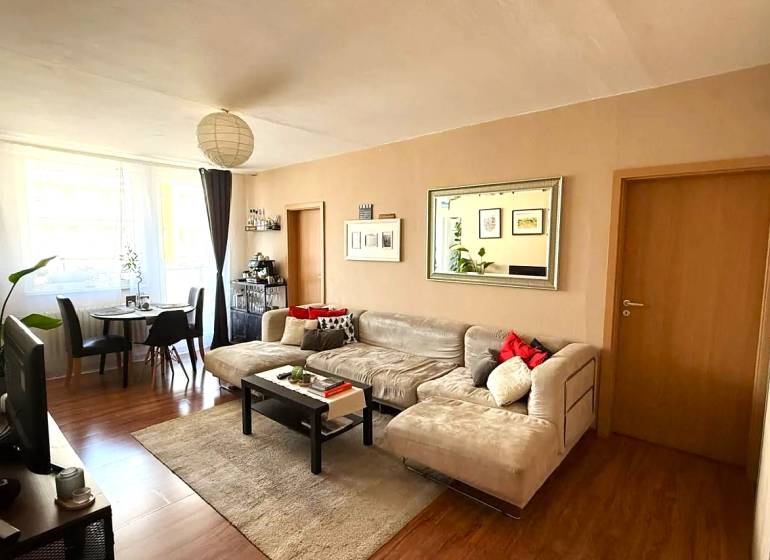 Pekný zariadený 3 izbový byt s lodžiou, Púpavová ulica, BA.Karlova Ves - Obývačka v 3-izbovom byte s podlahou s dreveným dekorom, sedačkou a jedálenským stolom.