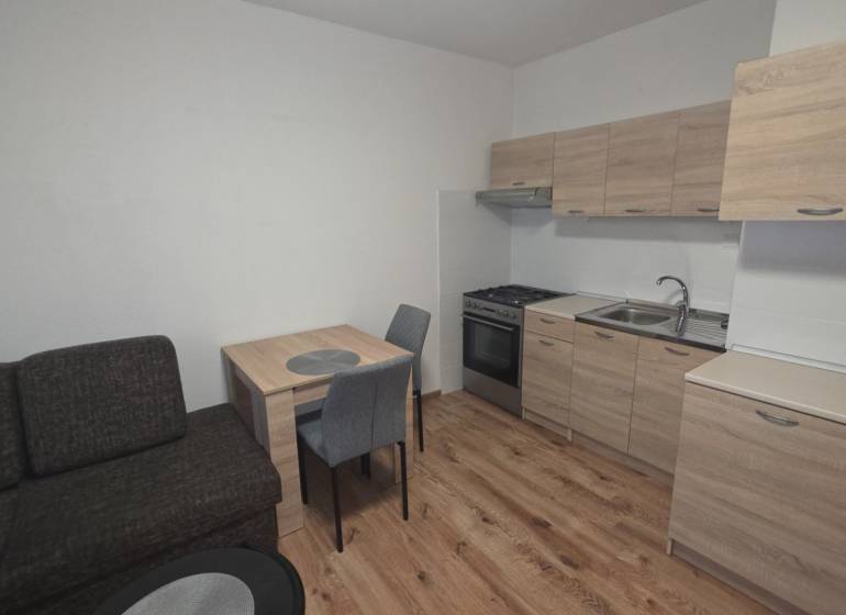 Prenájom veľký 1 izbový byt 48m2 Vráble- Centrum - Kuchyňa v 1-izbovom byte s dreveným dekorom podlahy a nábytku.