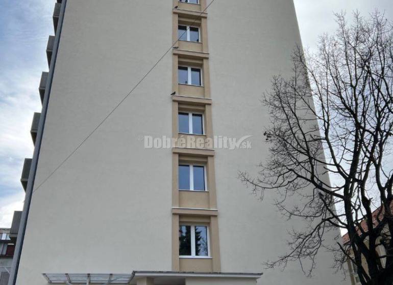 Nový nájomné 1 izbové byty v Prievidzi - ihneď k dispozícii - Bytová budova v Prievidzi na ulici T. Vansovej, pri ktorej parkuje oranžové auto.