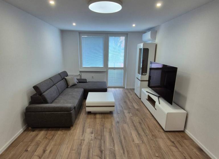 Prenájom 2-izbového bytu Bratislava II, Ružinov - Obývačka v 2-izbovom byte so sedačkou, stolíkom a televízorom na drevenej podlahe.