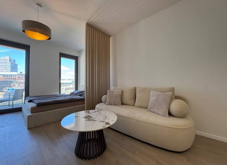 Prenájom 1-izbový byt s balkónom, METROPOLIS, Bratislava- Staré Mesto - Obývačka s pohovkou, konferenčným stolíkom a posteľou v 1-izbovom byte s podlahou s dreveným dekorom.