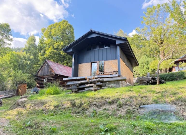 Chata pred dokončením, pozemok 770 m2, Horná Maríková - Chata v Hornej Marikovej, obklopená prírodou a drevenými stavbami, za slnečného dňa.
