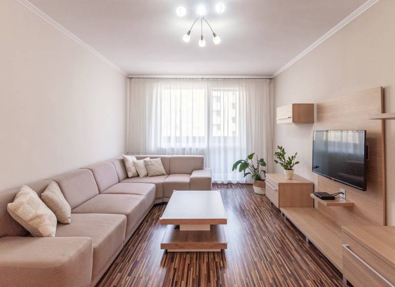 Predaj 3i bytu 84m2 - dva balkóny , Nábrežná v NZ - Obývacia izba so sedačkou, podlahou s dreveným dekorom a dekoráciami v 3-izbovom byte.