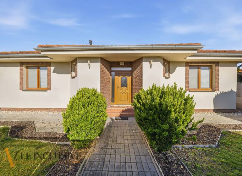 Na predaj 4-izb. rodinný dom s garážou, Kútniky - Rodinný dom v Kútnikoch s kríkovou výsadbou, bielou fasádou a hnedými doplnkami.