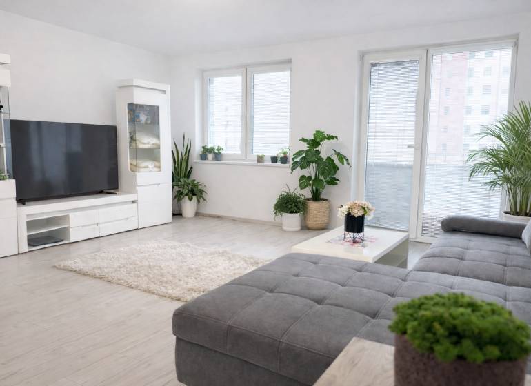 NOVOSTAVBA (2019) + PARKOVANIE | 2-izbový byt 69 m² – Bratislava - Obývacia izba v 2-izbovom byte s rastlinami a nábytkom na podlahe s dreveným dekorom.