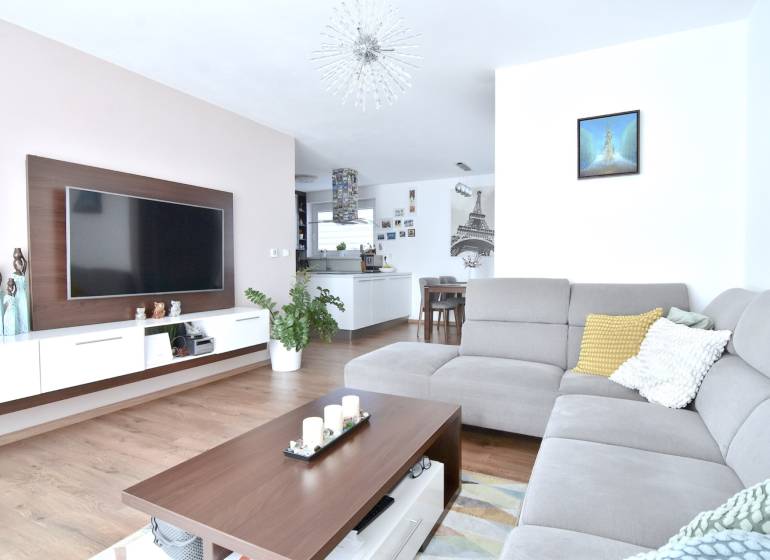 UHLISKÁ, 3-i byt, 80 m2 – zariadená novostavba s parkovaním v cene - Obývacia izba v 3-izbovom byte s podlahou s dreveným dekorom a sivou sedačkou.