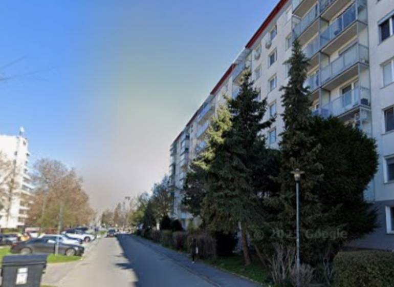 Garzónka, Jašíkova, Ružinov, pôvodný stav - Bytový dom v Bratislave - Ružinove na Jašíkovej ulici pri ceste s autami a stromami.