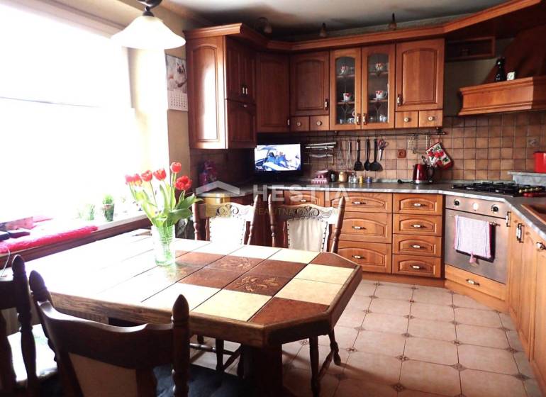 ZNÍŽENÁ CENA Veľký 2-izbový investičný byt Senica - 73,54 m² - Kuchyňa s dreveným dekorom, jedálenským stolom a kvetmi v 2-izbovom byte.