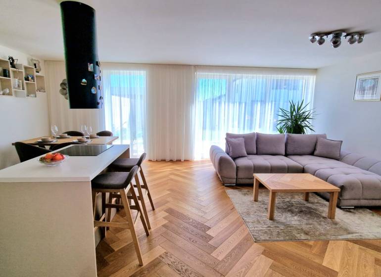 PRENÁJOM - 4 izbový rodinný dom, ktorý je súčasťou dvojdomu   - Obývačka v rodinnom dome s pohovkou, barovými stoličkami a podlahou s dreveným dekorom.