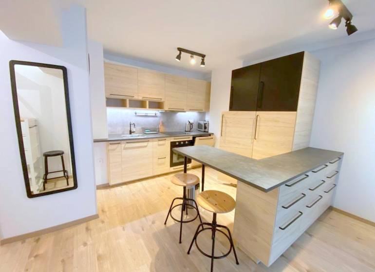 ŠTÝLOVÝ 2i byt, NOVOSTAVBA, BALKÓN, PARKIN, Paričková ulica, NIVY - Kuchyňa v 2-izbovom byte na Páričkovej s drevenými skriňami a barovým pultom.