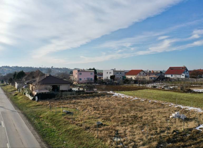 NA PREDAJ Stavebný pozemok v obci Golianovo - Pohľad na obytné pozemky v Golianove so zasneženými trávnatými plochami pri ceste.