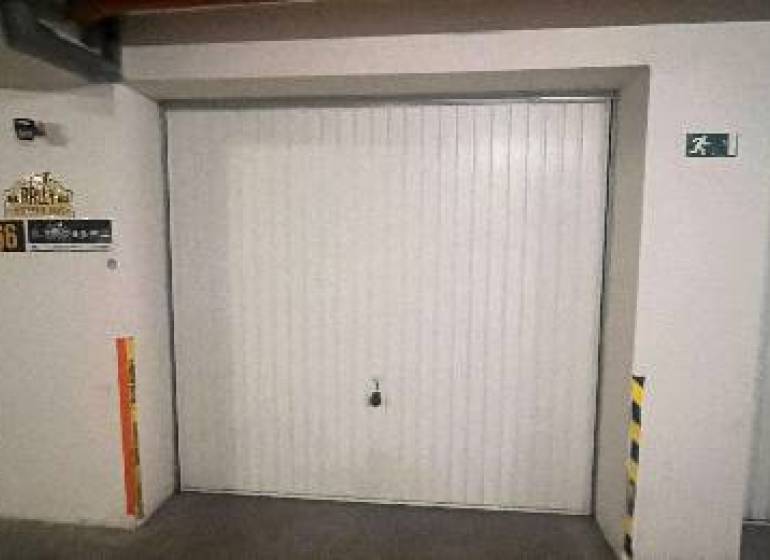 Garáž na prenájom. - Garáž v interiéri s bielymi dverami a bezpečnostnými značkami.