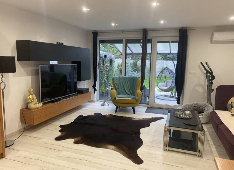 Na predaj: 3-izbový rodinný dom na predaj v obci Lesné Kračany - Obývacia izba v rodinnom dome s televízorom, dekorom Buddhu a terasovým výhľadom.