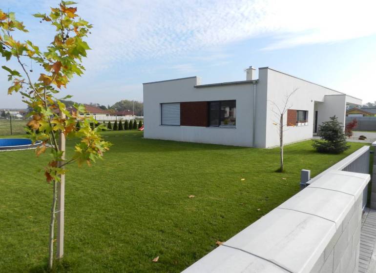 4.ETAPA!!! MODERNÁ NOVOSTAVBA - 4 izbový nízkoenergetický bungalov vys - Rodinný dom s bazénom na trávnatom dvore obklopený záhradou a veľkými oknami.
