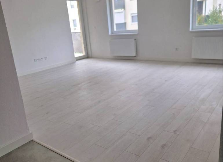 NOVOSTAVBA! Krásny, moderný a priestranný 3-izbový byt s veľkou logiou - Veľká svetlá izba s podlahou s dreveným dekorom v 3-izbovom byte.