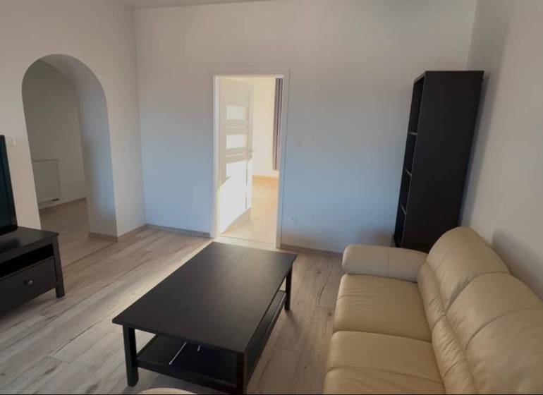 Prenájom 2-izbového bytu, Dunajská Streda - Obývacia izba s podlahou s dreveným dekorom v 2-izbovom byte, krémová sedačka a TV.