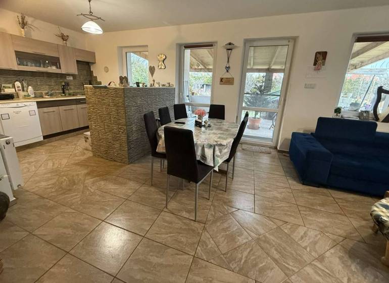 Predaj rodinného domu, Dunajská Streda - Jedáleň v rodinnom dome so stolom, kuchynskou linkou a obývačkou so sedačkou.