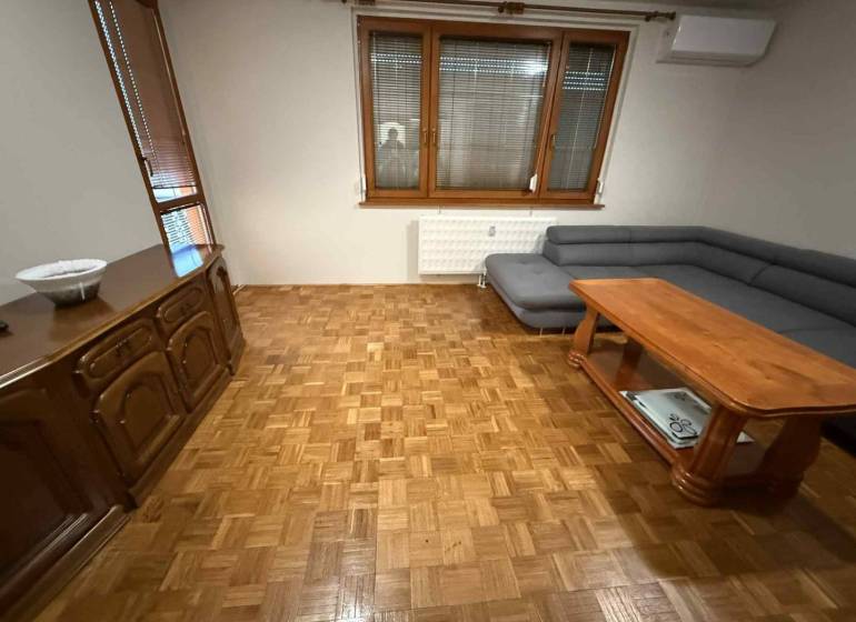 Prenájom 3-izbového bytu, Dunajská Streda - Obývacia izba v 3-izbovom byte s podlahou s dreveným dekorom, sedačkou a stolom.