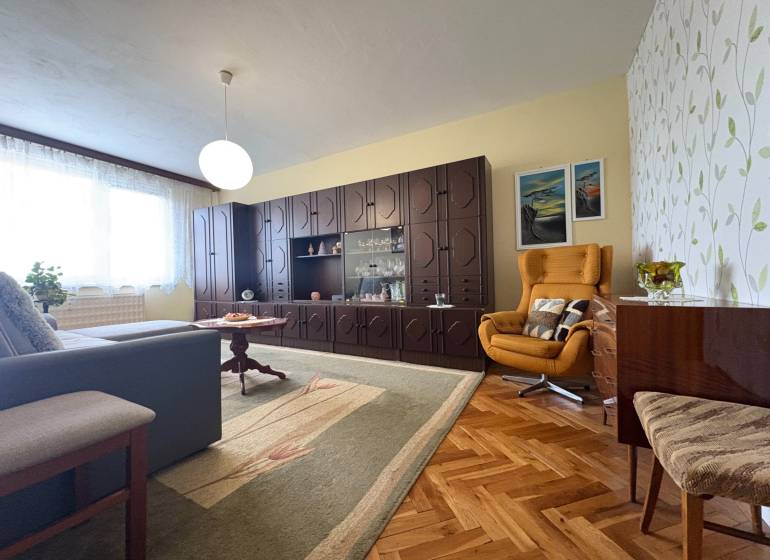 Na predaj: CENTRUM veľký 3 izb.byt + BALKON + ŠATNIK - Obývačka v 3-izbovom byte s rustikálnym nábytkom, drevenou podlahou a pohodlným kreslom.