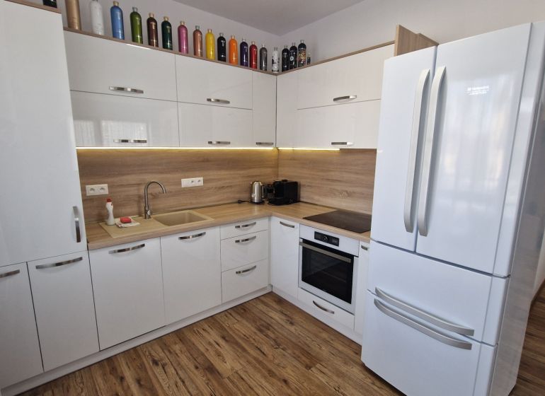 Rekreačný apartmán Vys. Tatry- HREBIENOK RESORT I. - 92 m2 -3-izbový - Kuchyňa v rekreačnom apartmáne s bielymi skrinkami a podlahou s dreveným dekorom.